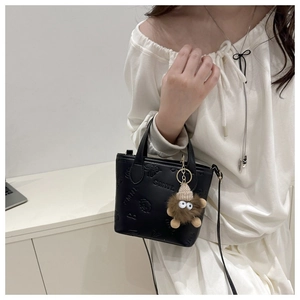 Detail of black crossbody bag with SMNL embossed texture and brown monster plush charm