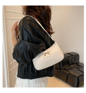 Detail of white lychee-grain leather underarm bag with golden bow hardware buckle