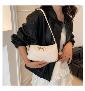 Macro detail of white lychee leather texture and golden bow hardware on underarm bag
