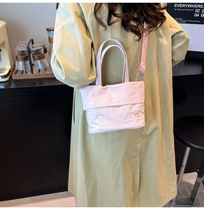 Détail du sac seau en toile plissée rose clair avec logo et bandoulière amovible