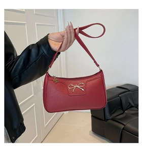 Dettaglio borsa sottobraccio rossa in pelle con fiocco dorato e ciondolo a fiore
