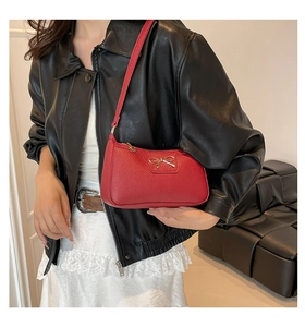 Detail of red pebbled leather underarm bag featuring a golden metal bow decoration