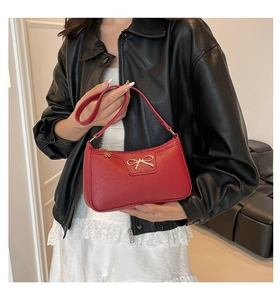 Detail of red pebbled leather baguette bag with a gold metal bow ornament and zipper
