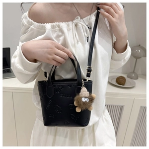 Detail of black leather crossbody bucket bag with butterfly embossing and plush monster charm