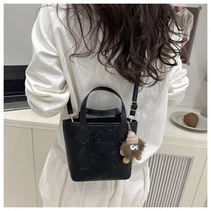 Detailed view of black bucket bag with SMNL embossing and cute brown plush charm