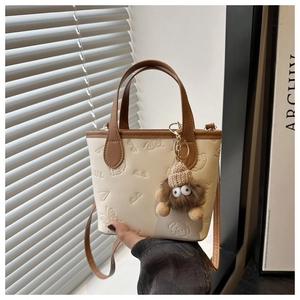 Detail of cream-colored bucket bag with embossed patterns and plush monster charm