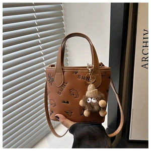 Detailed view of brown PU bucket bag featuring embossed patterns and a plush monster charm