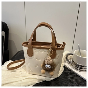 Detail of embossed cream bucket bag with brown handles and plush monster charm decoration