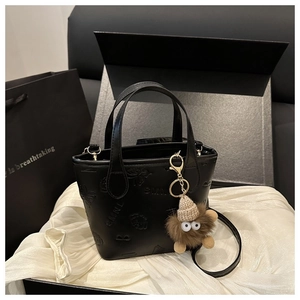 Detail of black leather tote bag with 3D embossed patterns and brown plush monster charm
