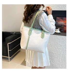 Detail of a large white tote bag with embossed cartoon patterns and green handles on a model
