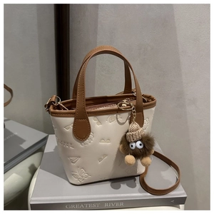 Detail view of cream-colored bucket bag with embossed patterns and monster charm accessory