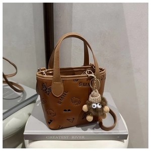 Detail of embossed patterns and brown plush monster charm on trendy crossbody bucket bag