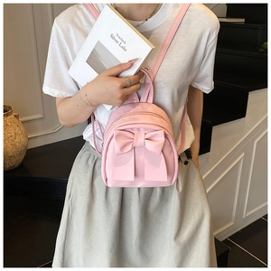 Pink mini nylon backpack with a large bow detail shown on a model in a stairwell