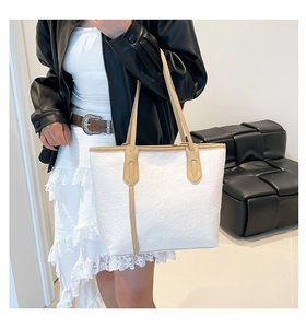 Detail of white embossed tote bag with floral patterns and beige shoulder strap worn by model