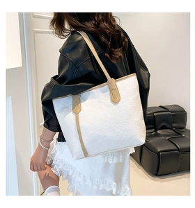 Detail of white leather tote bag featuring embossed cartoon patterns and soft tan handles