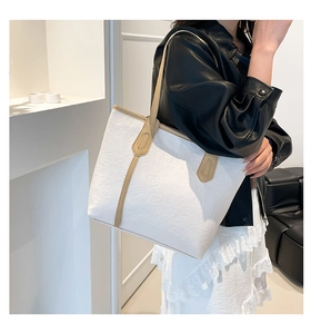 Detail of white tote bag featuring cartoon embossed texture and brown shoulder straps
