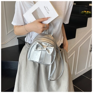Detail showing a silver mini backpack with a large bow on a model in a stylish setting