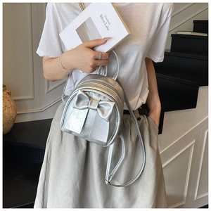 Detail of silver mini backpack with metallic bow and adjustable straps on a model