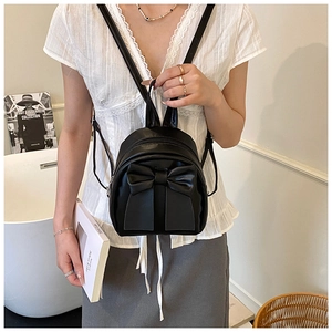Detail of a black leather mini backpack featuring a large bow and adjustable straps