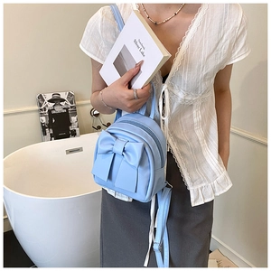 Detail of light blue mini backpack featuring a large bow and adjustable straps on a model