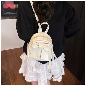 Close-up of white mini backpack with a large bow detail and elegant faux leather texture