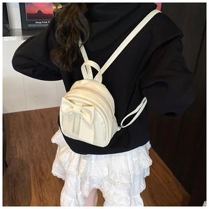 Mini cream backpack with large bow detail shown on model in a stylish street setting