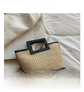 Détail du sac cabas en paille tissée avec poignées noires sur un tapis en maille blanc