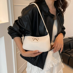 Borsa a spalla bianca in pelle lychee con fiocco dorato indossata su giacca nera