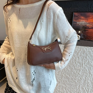 Borsa sottobraccio in pelle marrone con fiocco dorato indossata da una modella