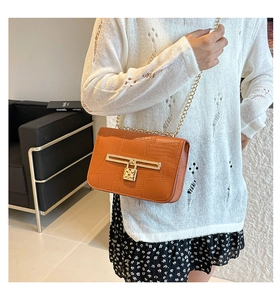 Close-up of orange-brown croc-embossed leather texture with golden chain strap and lock