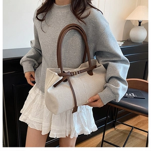Detail of cream canvas tote bag featuring brown leather handles and buckle accents