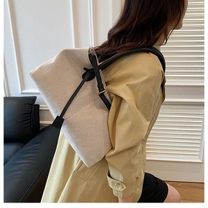 Close-up of beige canvas tote bag with black leather trim and gold hardware on model