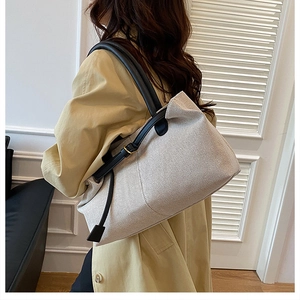Close-up of cream canvas tote bag with black leather straps and gold buckle detail
