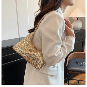 Detailed side view of a gold sequin baguette bag worn by a model in a minimalist setting