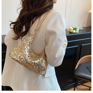 Close-up of golden sequined crescent bag with leather strap on a white blazer