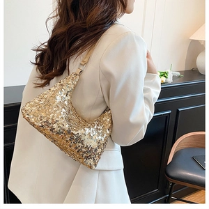 Close-up of a gold sequined crescent moon bag worn by a model in a white blazer