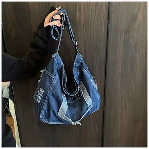 Detail of distressed denim crossbody bag showing frayed edges and vintage metal buckle