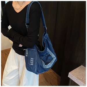 Detailed side view of dark blue denim hobo bag with distressed frayed edges and wide strap