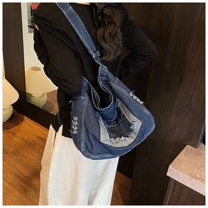 Detail of frayed edge texture on deep blue denim crossbody bag with wide strap