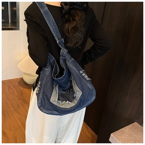 Detail of blue denim messenger bag with distressed edges and metal buckle strap