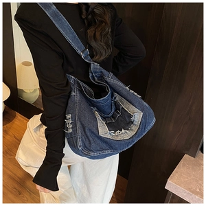 Detail view of large denim patchwork tote bag with frayed edges worn by a model