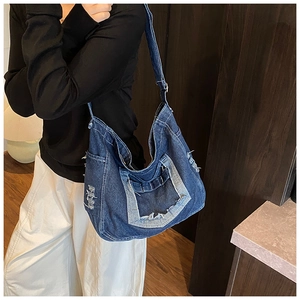 Detail of dark blue denim tote bag with frayed edges and adjustable wide shoulder strap