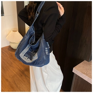 Detail of distressed denim shoulder bag featuring ripped fringes and adjustable metal buckle