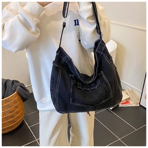 Detail of black denim messenger bag featuring white contrast stitching and frayed edges