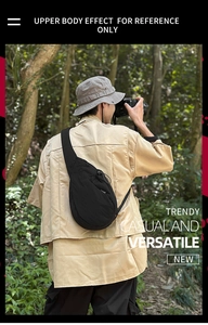 Outdoor shot of a black nylon crossbody bag featuring an adjustable strap and mesh pocket