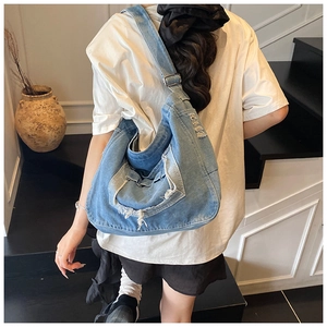 Detail of distressed denim crossbody bag with raw edges and functional front pocket