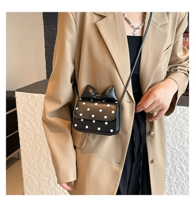 Close-up of a mini black polka dot handbag with a bow detail on a tan blazer outfit