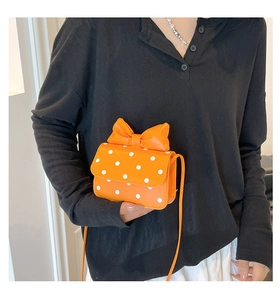 Detail of a bright orange polka dot mini crossbody bag with a 3D bow accent on the flap