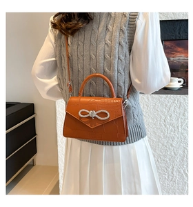 Détail du sac orange à motif crocodile avec une boucle papillon ornée de strass brillants