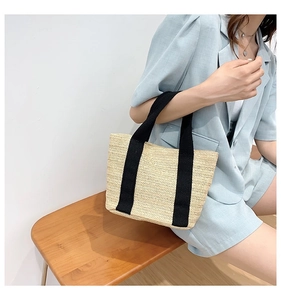 Close-up of woven straw tote bag with black canvas straps on a minimalist setting